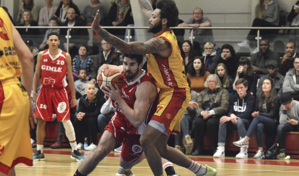 Magne i rød drakt med ballen under en basketballkamp